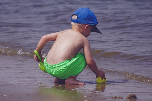 在海边玩的蓝帽子和绿色短裤的男孩 · 免费素材图片
