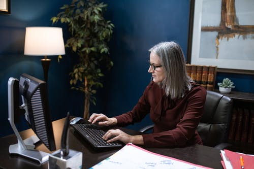 坐在桌前使用便携式计算机的棕色长袖衬衫的女人 · 免费素材图片