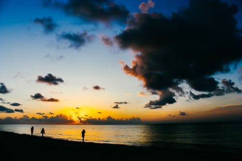 人们在日落时站在海边 · 免费素材图片