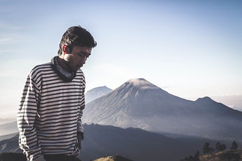 身穿白色和黑色条纹运动衫的人站在山前 · 免费素材图片