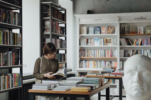 一个女人在书店里翻阅一堆书 · 免费素材图片