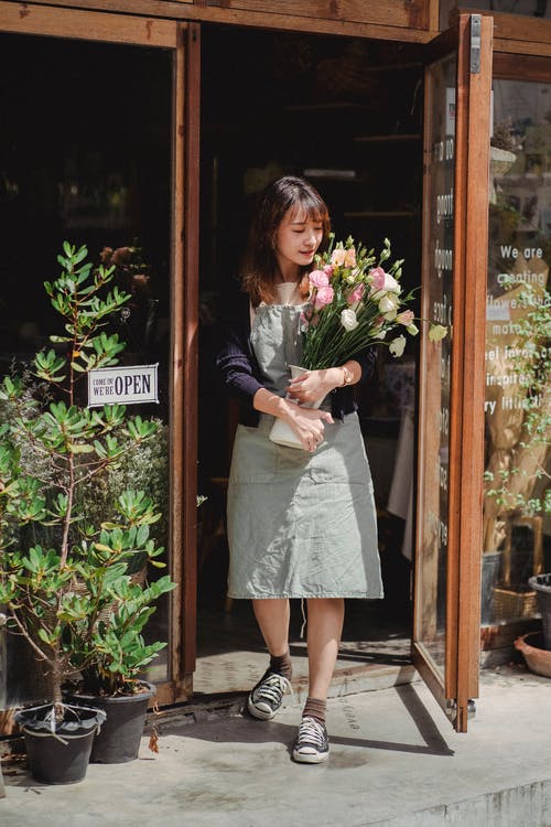 站立与花束的正面亚裔女性卖花人在商店门道入口 · 免费素材图片