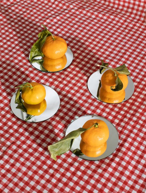 橘子放在方格桌布的镜面上 · 免费素材图片