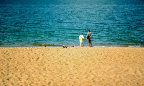 两个人站在海滩附近 · 免费素材图片