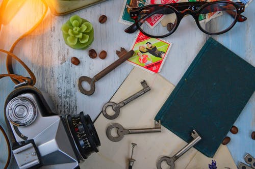 灰色相机，黑皮书和棕色镜框眼镜旁边的四个灰色万能钥匙 · 免费素材图片