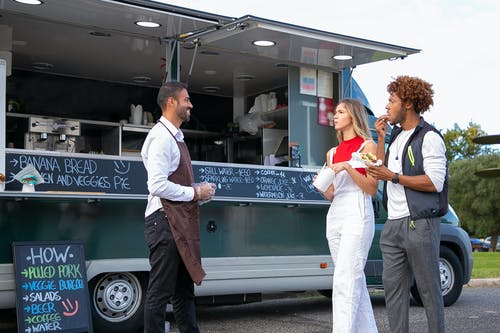 年轻多种族夫妇吃外卖快餐，走在民族厨师站在面包车附近 · 免费素材图片