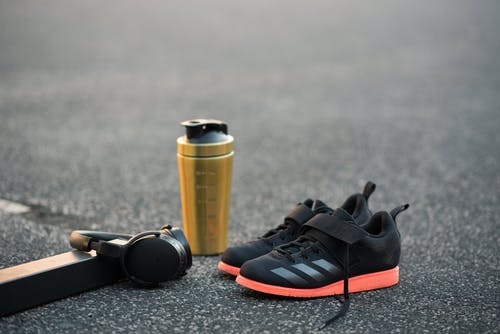 现代运动鞋附近健身瓶和人行道上的耳机 · 免费素材图片