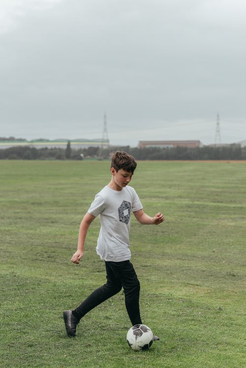 在绿色的原野中踢足球的男孩 · 免费素材图片