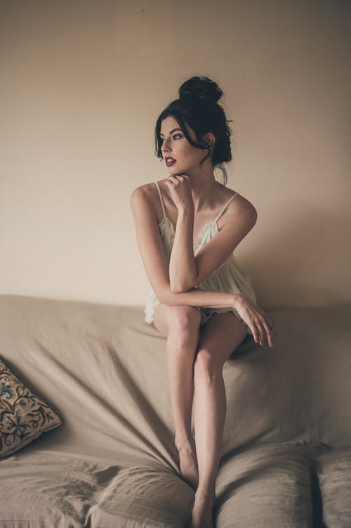 美丽的女人，穿着白色的晚礼服，坐在沙发的靠背上，看着别处的照片 · 免费素材图片