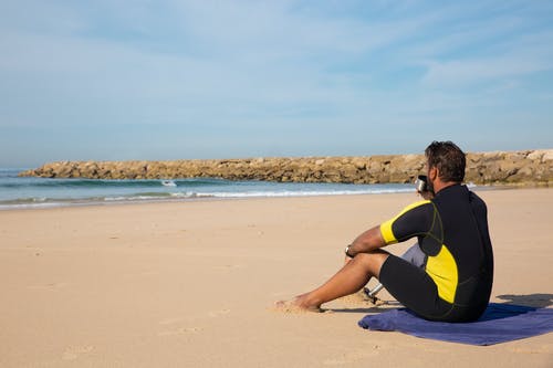 匿名男性截肢者喝饮料，在沙滩上休息 · 免费素材图片