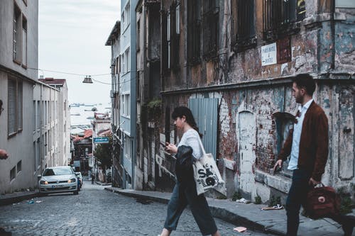 男人和女人过街与旧的废弃建筑在拐角处 · 免费素材图片