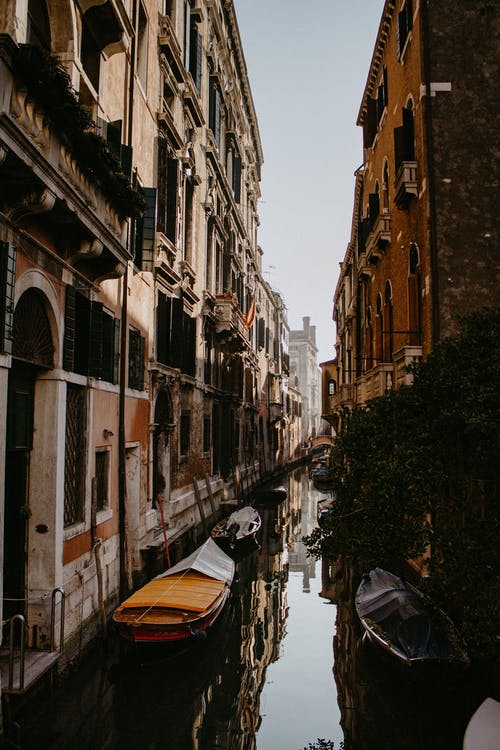 棕色和白色的小船，在建筑物之间的河上 · 免费素材图片