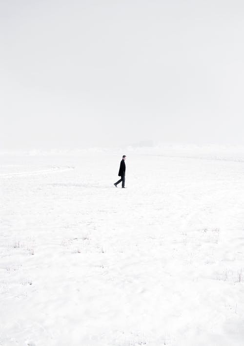 黑大衣的人在积雪覆盖的田野上行走 · 免费素材图片