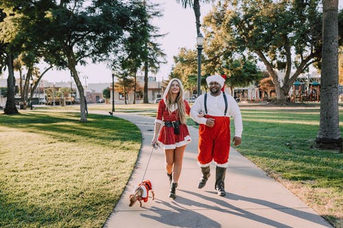 男人和女人在圣诞老人的衣服，在一条狗的具体途径上行走 · 免费素材图片