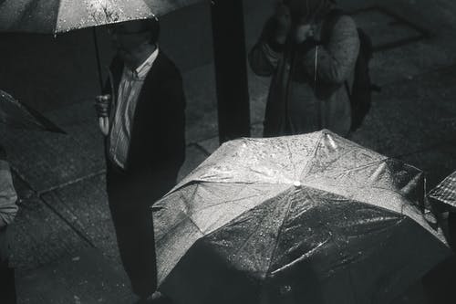 下雨时手持雨伞的男子的灰度照片 · 免费素材图片
