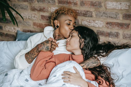 纹身黑女人躺在床上接吻同性恋女友 · 免费素材图片