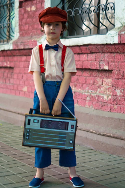 男孩拿着收音机，站在红房子旁边的照片 · 免费素材图片