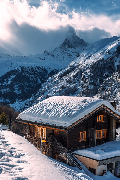 在白雪覆盖的山脉附近积雪地面上的棕色木屋 · 免费素材图片