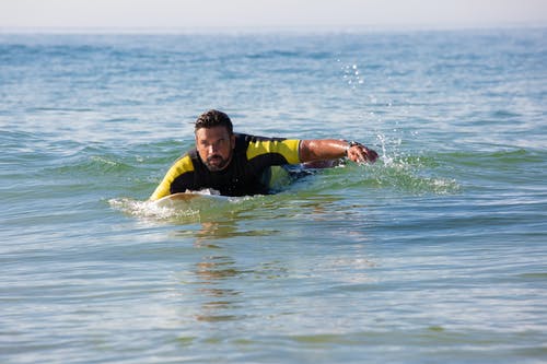 在海水上的冲浪板上漂浮的敬业族裔男性冲浪者 · 免费素材图片