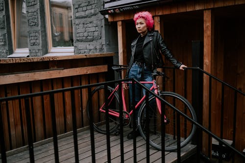 站在红色自行车旁边的黑夹克的女人 · 免费素材图片