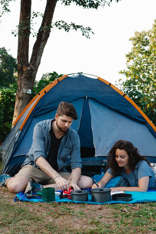 男人和女人坐在蓝色和橙色的圆顶帐篷 · 免费素材图片