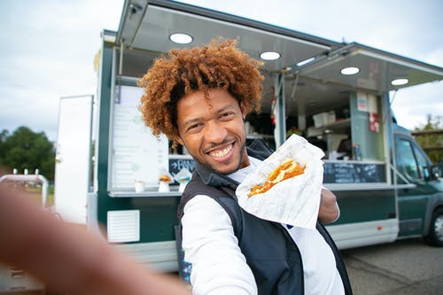 微笑着黑人吃汉堡和采取自拍照 · 免费素材图片