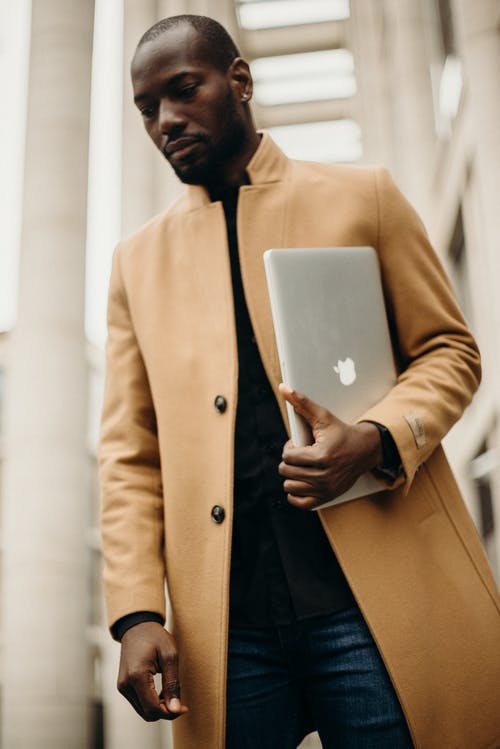 男子穿着橙色风衣，拿着银色的macbook Pro · 免费素材图片