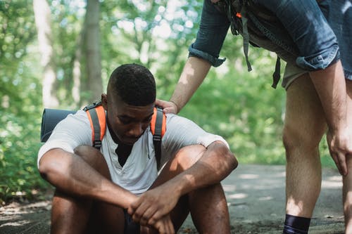 不开心的黑人徒步旅行者坐在森林的地面上 · 免费素材图片