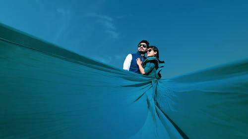 女人穿着蓝色马克西长裙拥抱男人在清澈的蓝天下 · 免费素材图片
