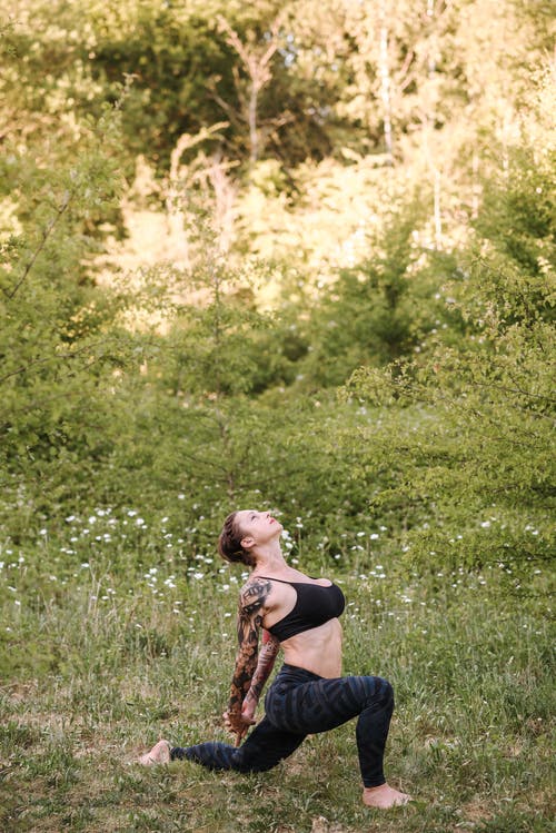 在草地上练习瑜伽时伸胳膊的纹身的女人 · 免费素材图片