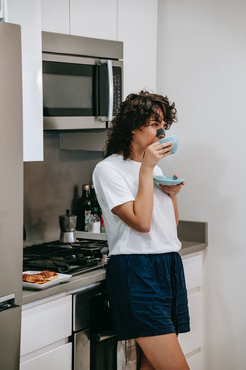 站在厨房水槽前的白衬衫和蓝色牛仔牛仔裤的女人 · 免费素材图片