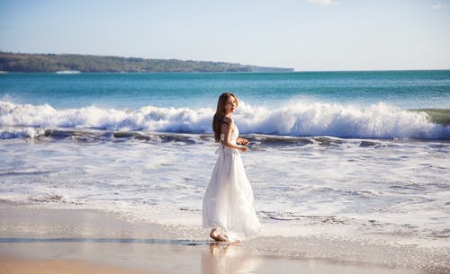 海滩上穿白裙子的女人的浅焦点照片 · 免费素材图片
