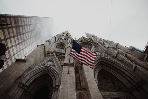 低角度摄影的棕色混凝土大教堂上挥舞着美国国旗 · 免费素材图片