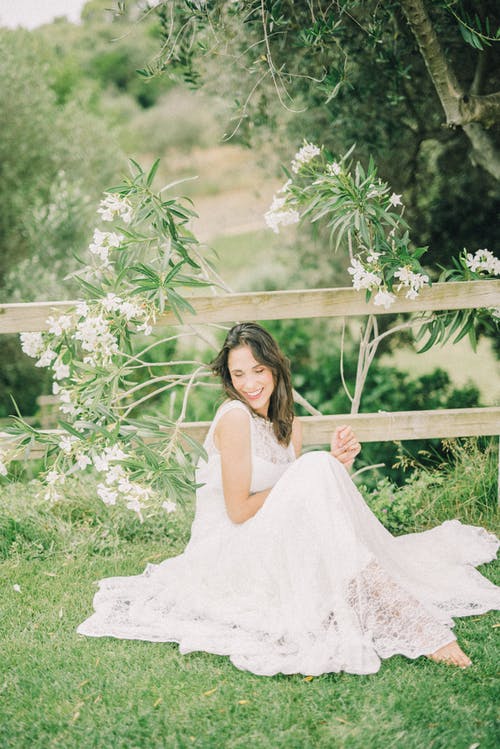 穿着婚纱时微笑着坐在草地上的女人 · 免费素材图片