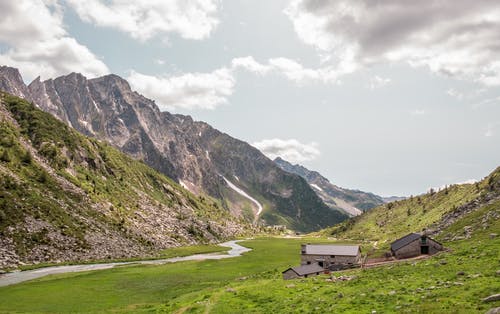 在多云的天空下山附近的绿草田 · 免费素材图片