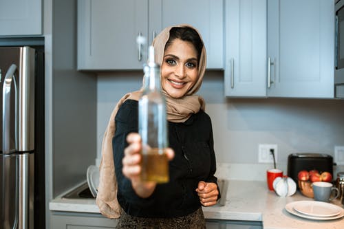 展示瓶油的快乐的种族妇女在厨房里 · 免费素材图片