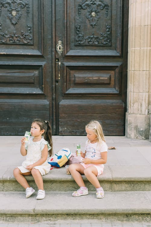 2个女孩坐在棕色的水泥地板上 · 免费素材图片