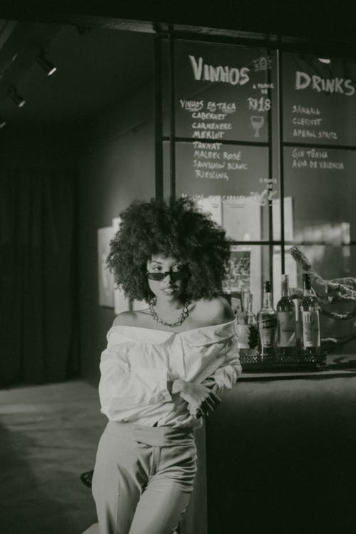 斜靠在酒吧柜台的露肩礼服摆姿势的女人的灰度照片 · 免费素材图片