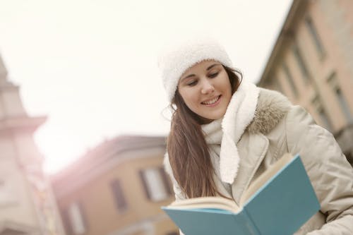 在大街上微笑的女人看书 · 免费素材图片