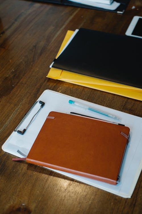 笔记本和剪贴板与论文放在桌上的文件夹和钢笔 · 免费素材图片