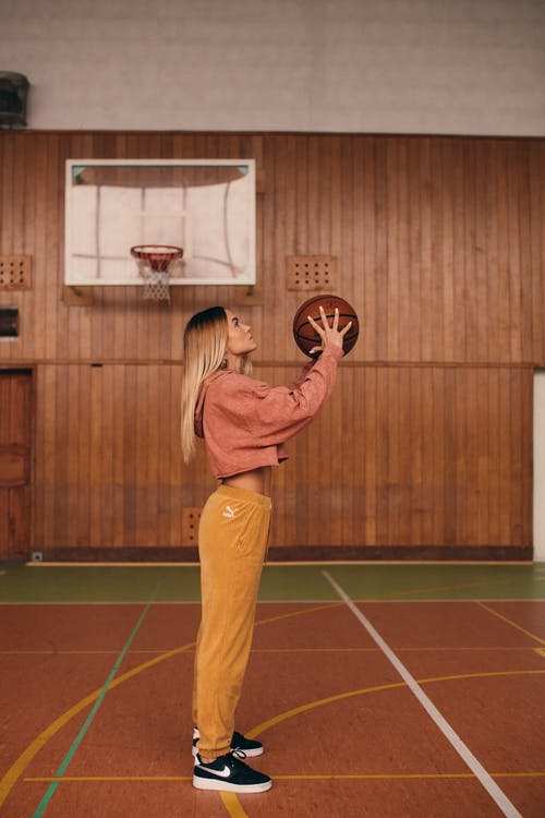 棕色长袖衬衫和棕色的裤子，站在篮球场上的女人 · 免费素材图片