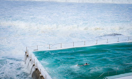 在海洋旁边的游泳池里游泳的人 · 免费素材图片