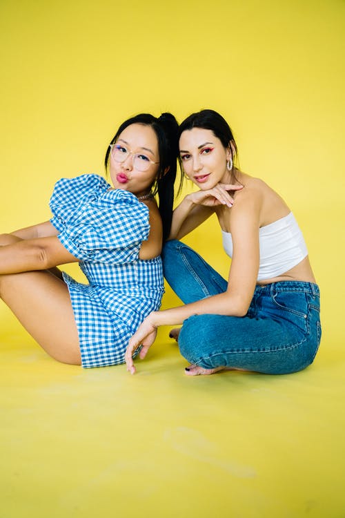 白色背心和蓝色牛仔裤的女人坐在蓝色和白色的女人旁边的女人 · 免费素材图片