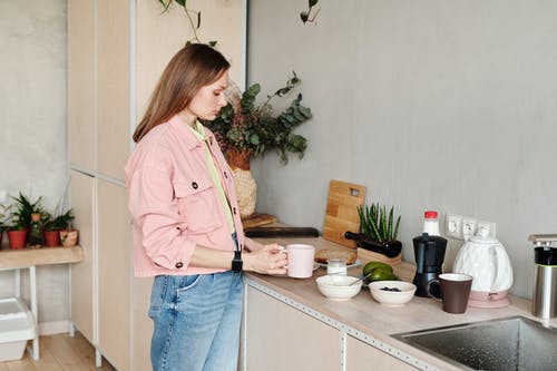 衬衫和蓝色牛仔牛仔裤，站在厨房的水槽旁的粉红色按钮的女人 · 免费素材图片