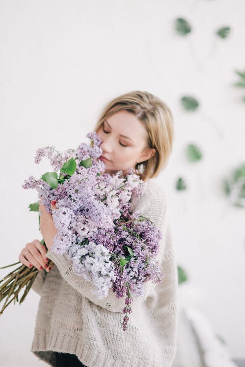 拿着紫色花的白色编织毛线衣的女孩 · 免费素材图片
