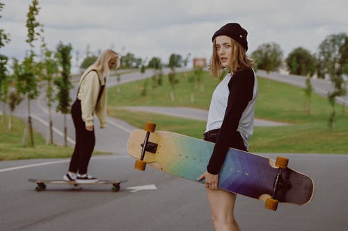 黑色和白色的长袖衬衫，拿着蓝色和黄色的滑板的女人 · 免费素材图片