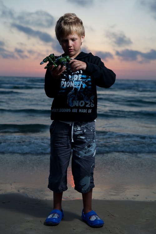 黑色连帽衫和蓝色牛仔牛仔裤，站在海滩上的男人 · 免费素材图片