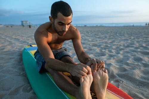 裸照男子坐在海滩上的蓝色冲浪板 · 免费素材图片