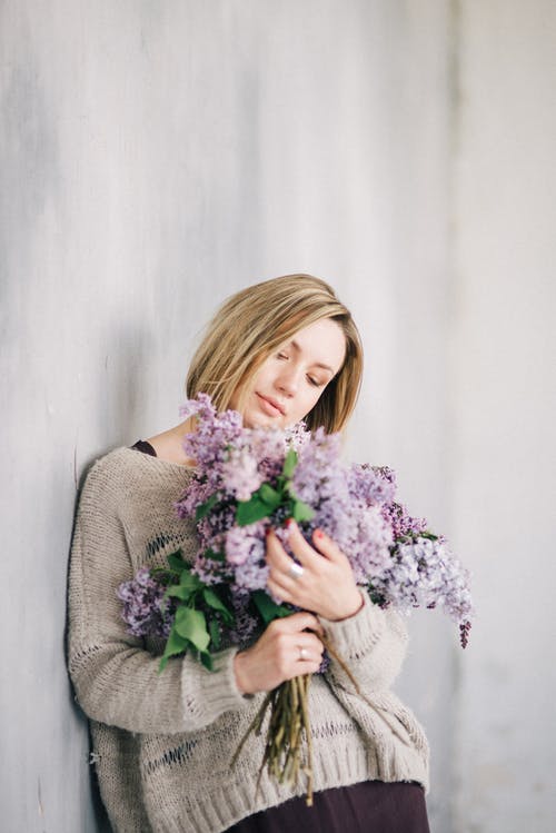 拿着紫色花的灰色针织毛衣的女人 · 免费素材图片