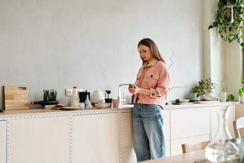 粉色长袖衬衫和蓝色牛仔牛仔裤，站在白色的木桌旁边的女人 · 免费素材图片